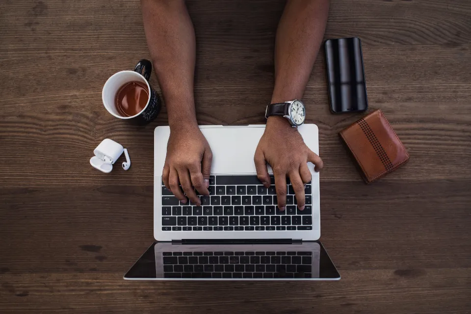 Hands typing on a laptop from above, on a wooden desk